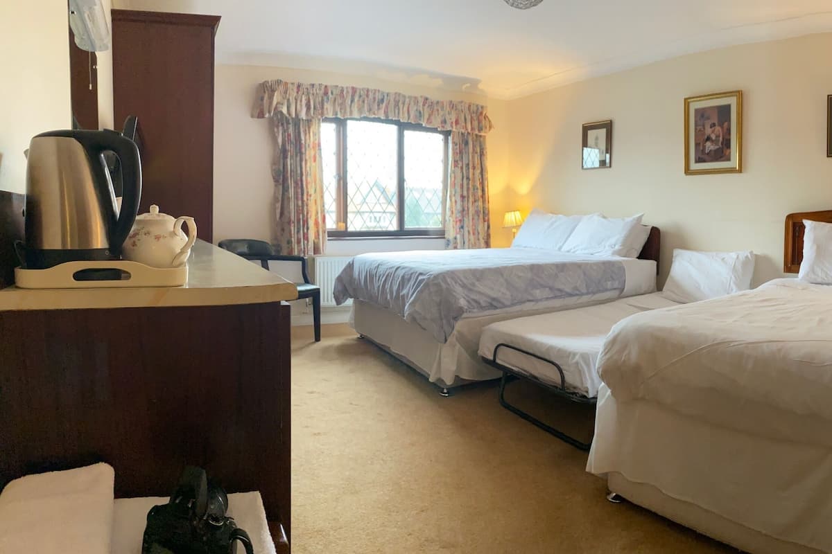 A hotel room with two beds, a desk with a kettle, and a window with curtains.