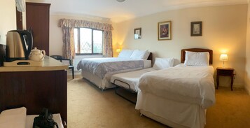 Habitación de hotel con dos camas, un escritorio con hervidor y ventana con cortinas.