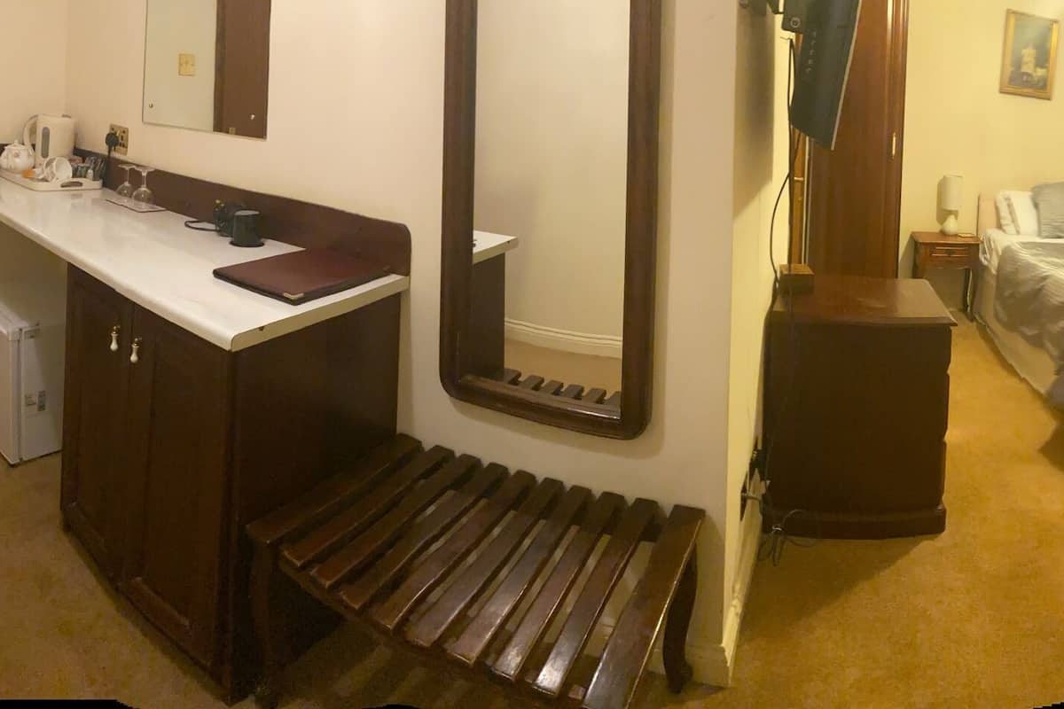 A hotel room with a bed, a desk with a chair, a small table with a chair, a mirror, and a window with curtains.