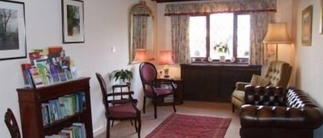Una sala de estar con un sofá de cuero oscuro, una estantería de madera, un tapete rojo y una ventana con cortinas.