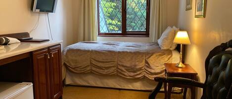 Una camera da letto con un letto, una scrivania con un computer, una sedia, una lampada e una finestra vista alberi.