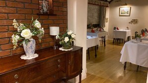Een eetgedeelte met houten tafels en stoelen, een bakstenen muur en een houten kast met decoratieve vazen.