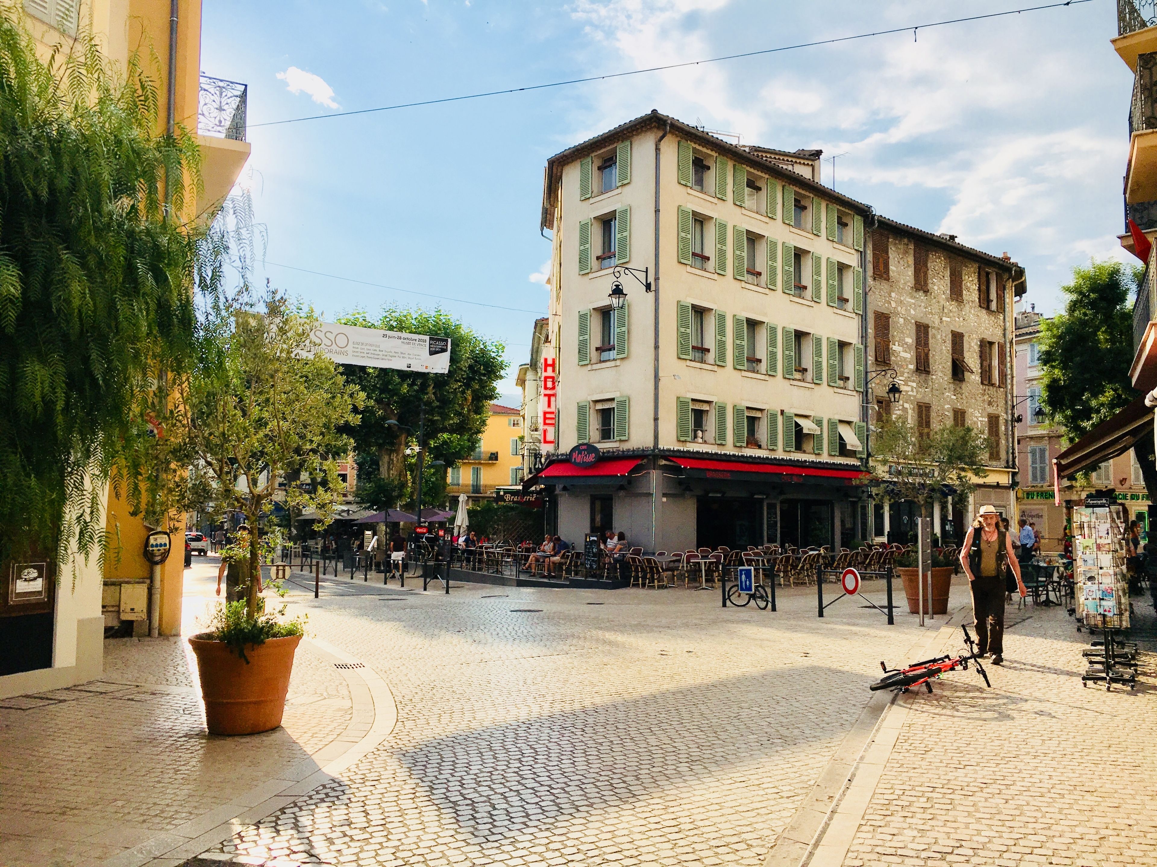 A hotel with a red awning, outdoor seating, and a cobblestone street.