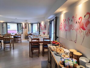 Un comedor con mesas y sillas de madera, un bufé con diversas opciones de comida, y una pared decorada con una pintura de flamenco.