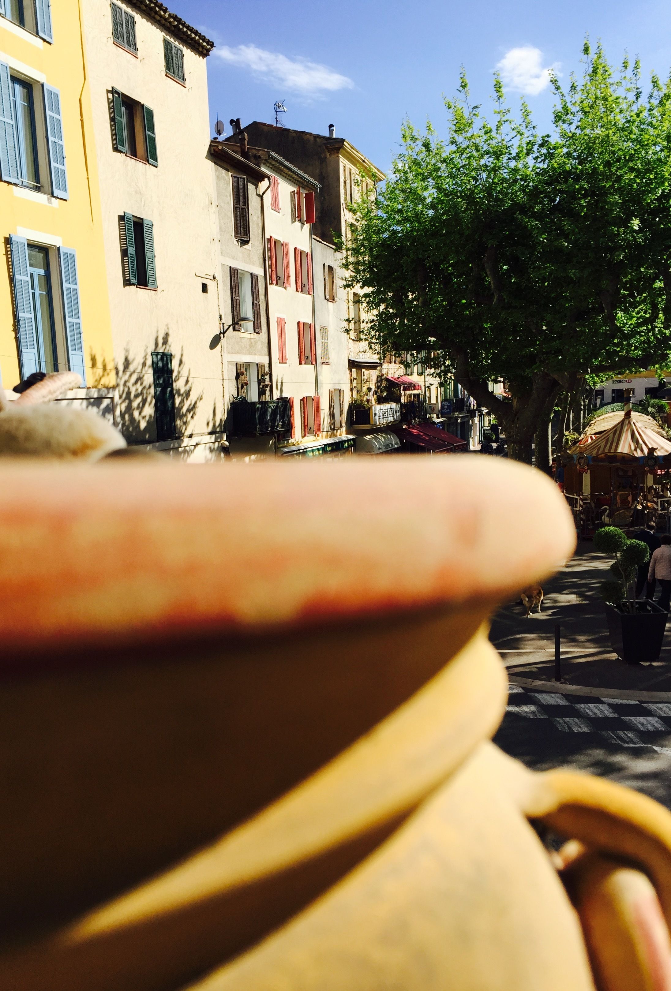 A street view with buildings, a tree, and a pot in the foreground.