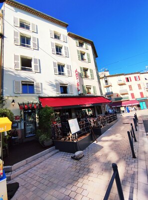 Un hotel con toldo rojo, mesas al aire libre y un cielo azul despejado.