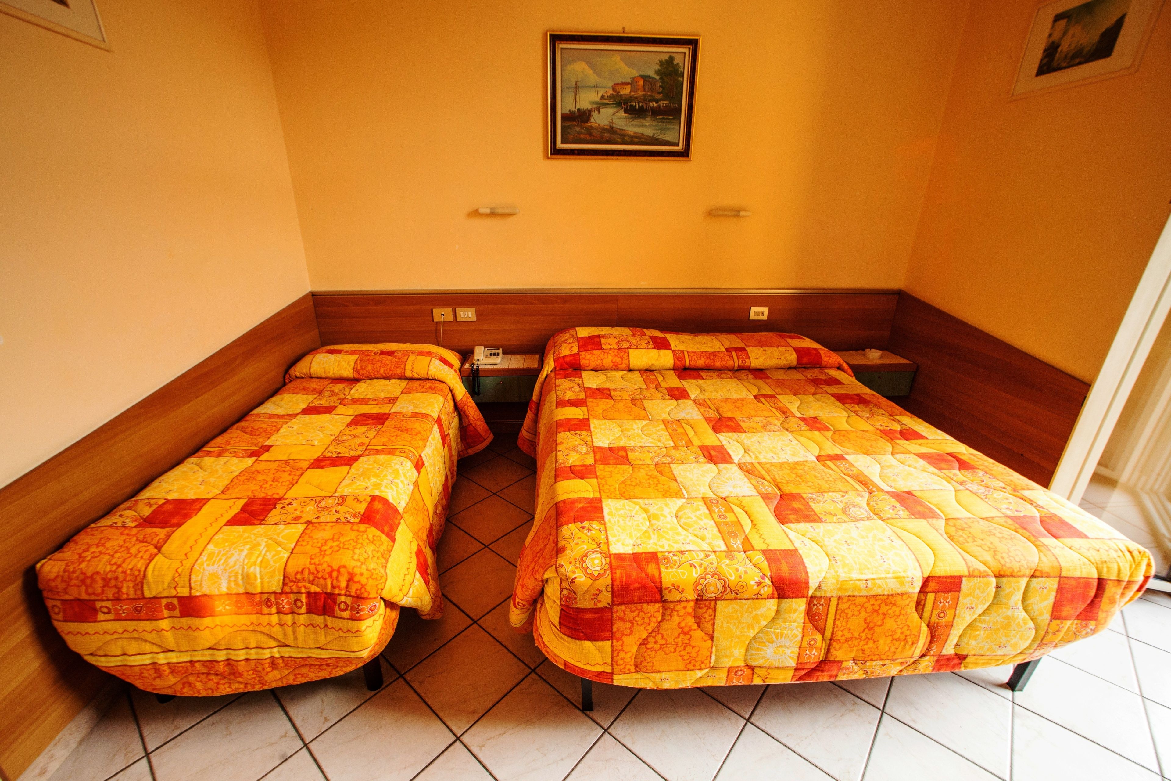 A room with two single beds, wooden headboards, a painting on the wall, and a tiled floor.