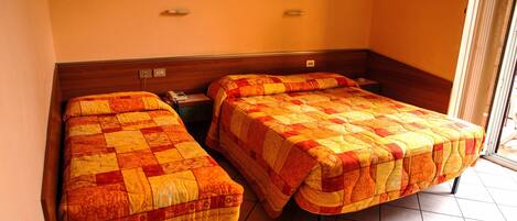 Habitación de hotel con dos camas individuales, cabecero de madera, un cuadro en la pared y suelo de baldosas.