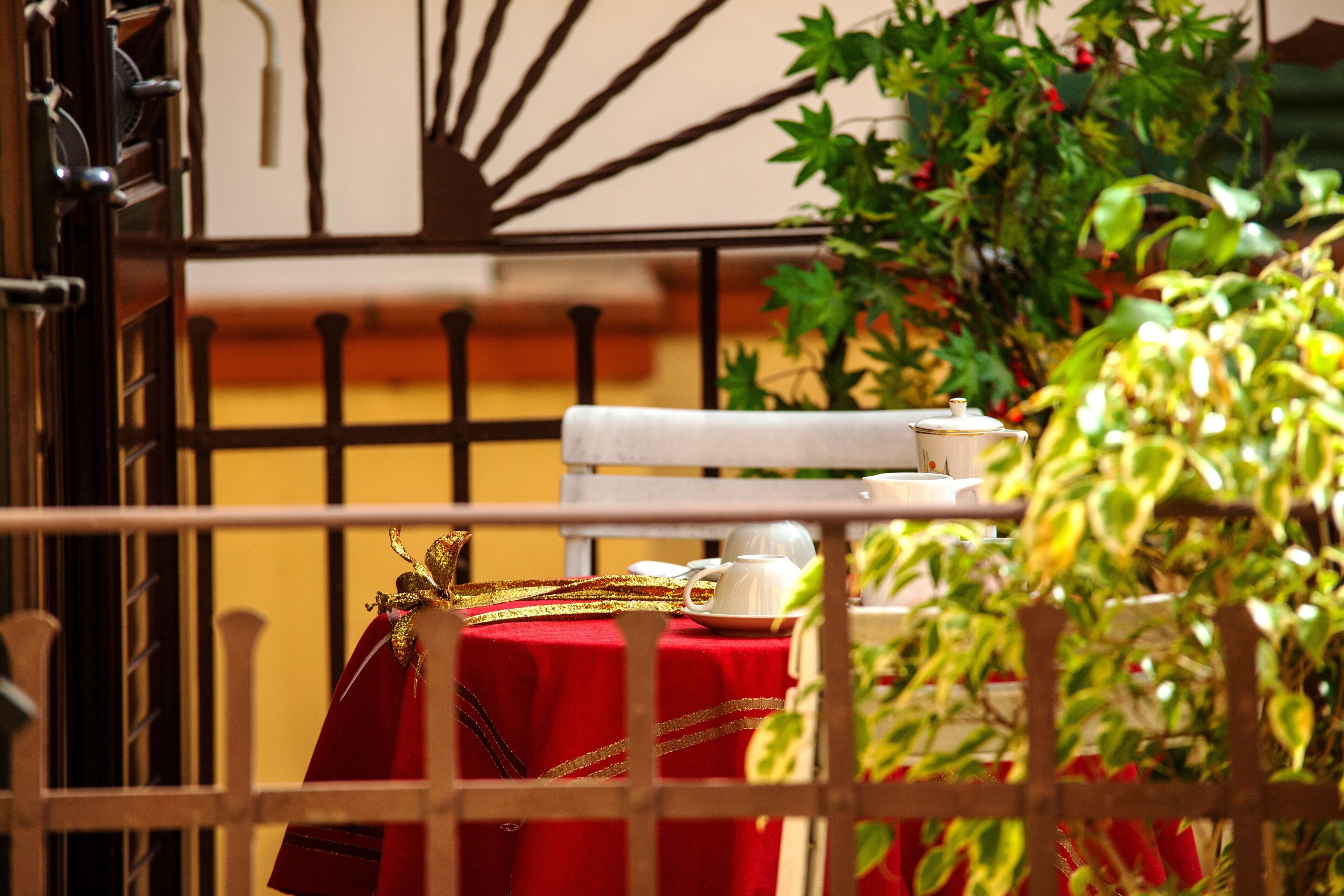 A balcony with a red tablecloth, a white chair, and a white table with a teapot and cup.
