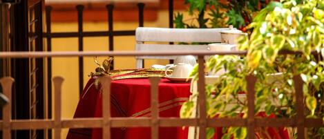 A balcony with a red tablecloth, a white chair, and a white table with a teapot and cup.