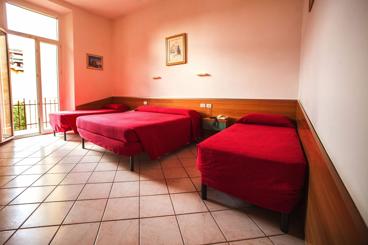 Une chambre d’hôtel avec deux lits, une tête de lit en bois, une fenêtre donnant sur un paysage agréable et une porte menant à un balcon.