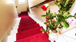A staircase with a red carpet, white walls, and a potted plant with flowers. - Hotel Villa Il Castagno (Florence)