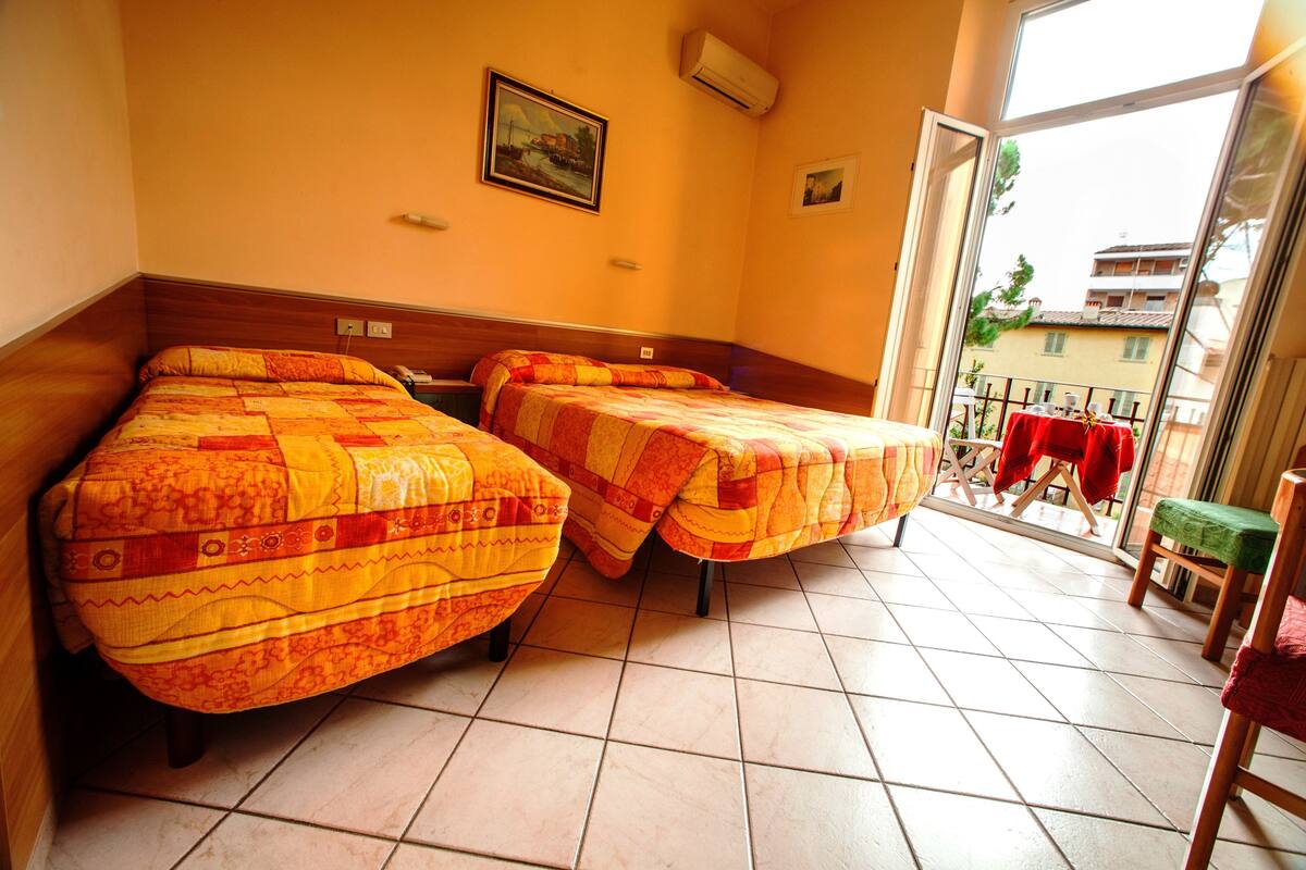 Une chambre d’hôtel avec deux lits, un balcon avec une table et des chaises, et une vue sur les bâtiments environnants.