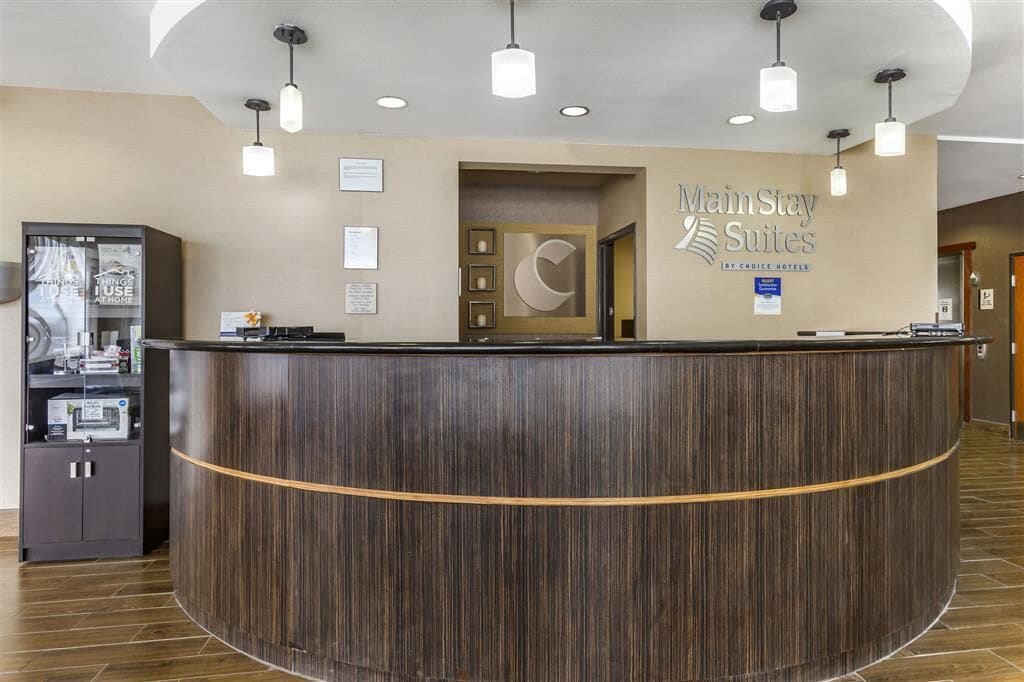 Un comptoir d’accueil en bois foncé, le logo de MainStay Suites et une enseigne indiquant qu’il fait partie du groupe Choice Hotels.