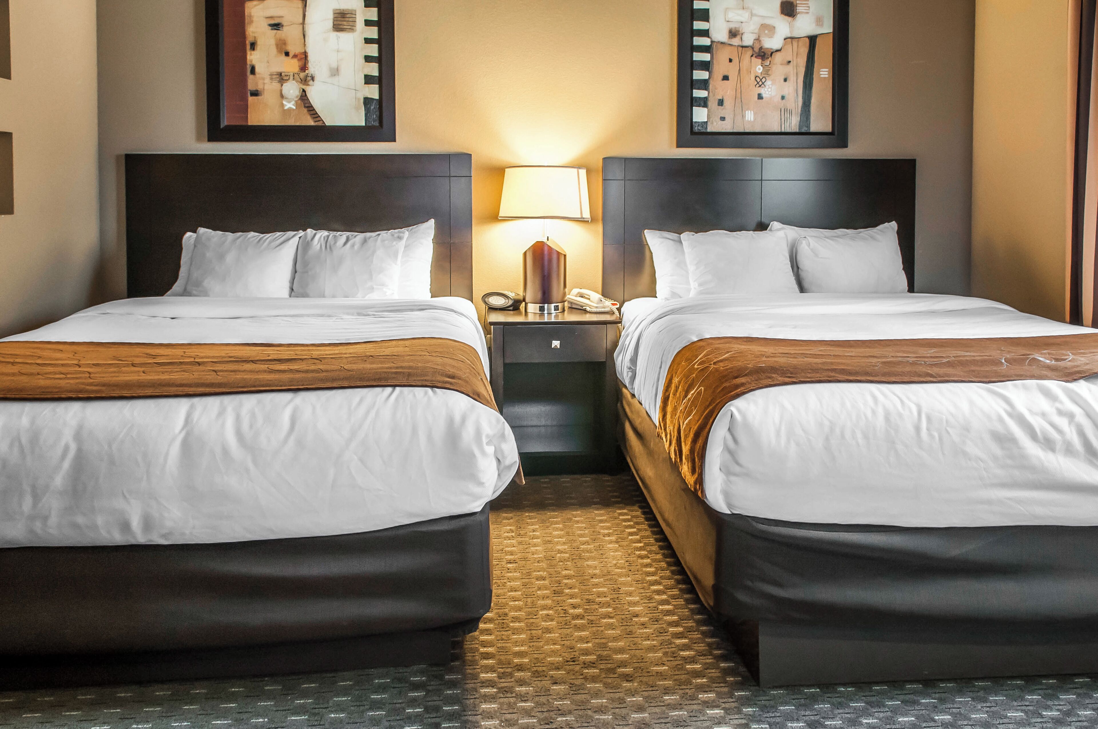 A hotel room with two beds, a nightstand with a lamp, and artwork on the walls.