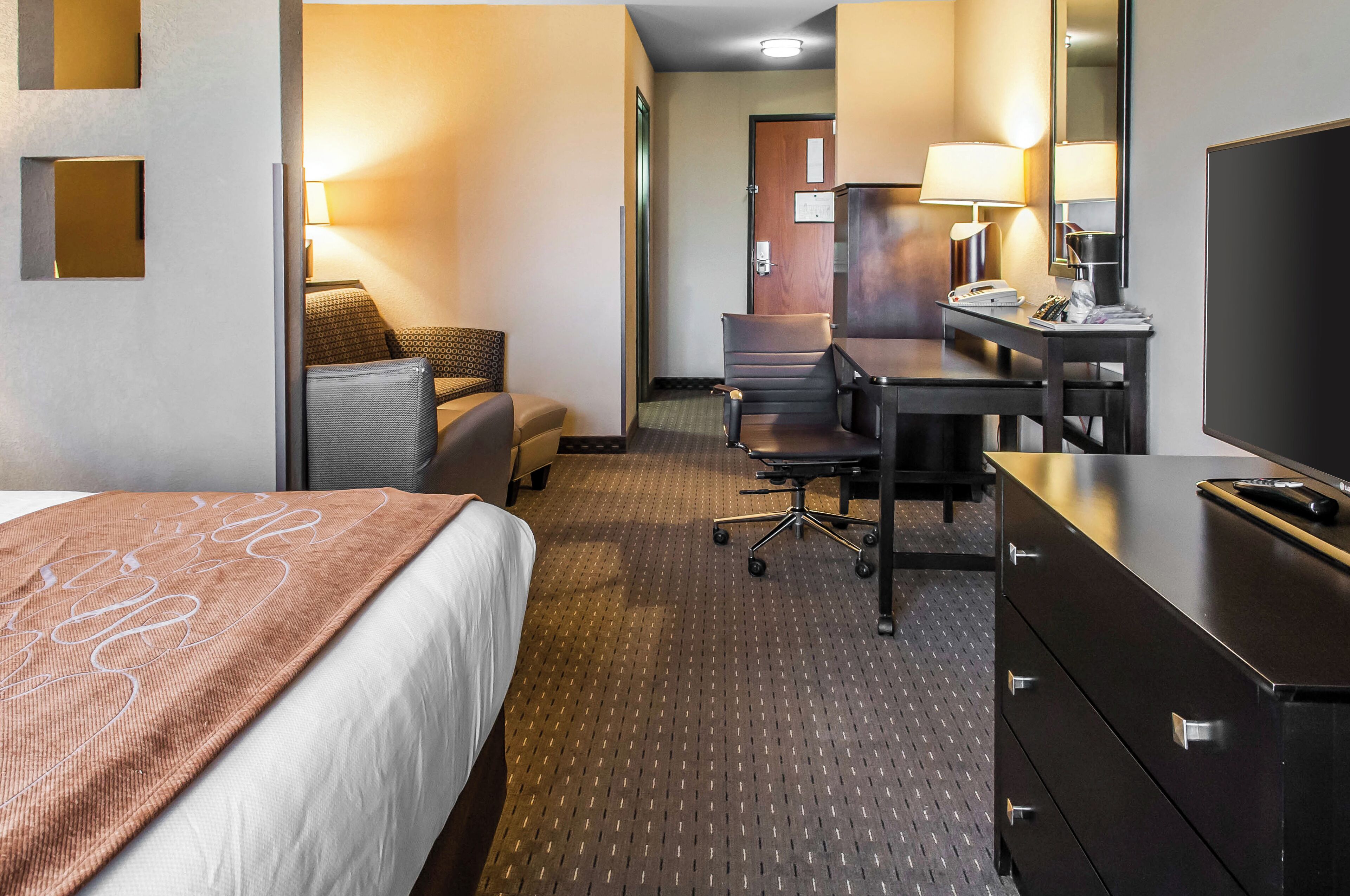 A hotel room with a bed, a desk, a chair, a dresser, and a television.