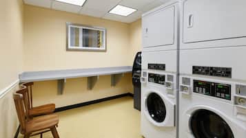 A laundry room with stacked washers and dryers, a wooden chair, and a window with blinds.