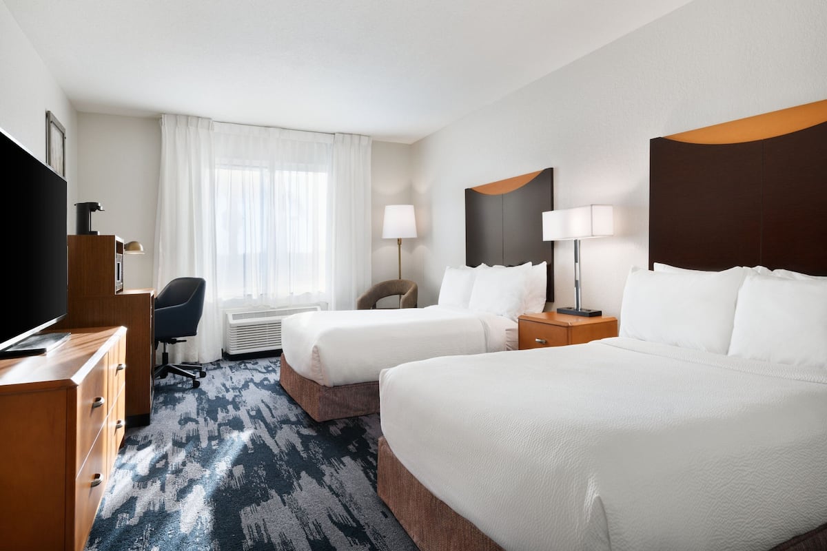 A hotel room with two beds, a desk, a TV, a chair, and a window with curtains.