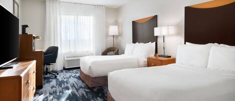 A hotel room with two beds, a desk, a TV, a chair, and a window with curtains.