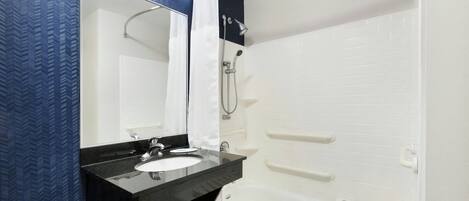 A modern bathroom with a black countertop sink, a large mirror, a white bathtub, and a shower area.