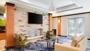 A modern living room with a stone wall, a flat-screen TV, a fireplace, and comfortable seating. - Fairfield Inn & Suites by Marriott Fort Pierce (Fort Pierce)