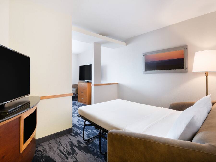 Quarto de hotel com cama, televisão, escrivaninha e abajur.