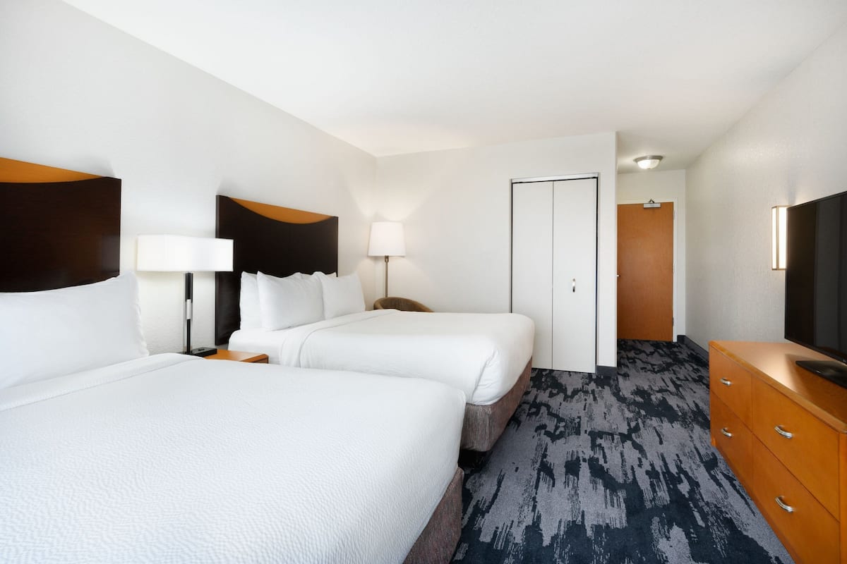A hotel room with two beds, a dresser, a TV, and a door leading to another room.