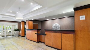 A hotel reception area with a modern design, featuring a reception desk, a large potted plant, and a sign indicating the hotel name. - Fairfield Inn & Suites by Marriott Fort Pierce (Fort Pierce)