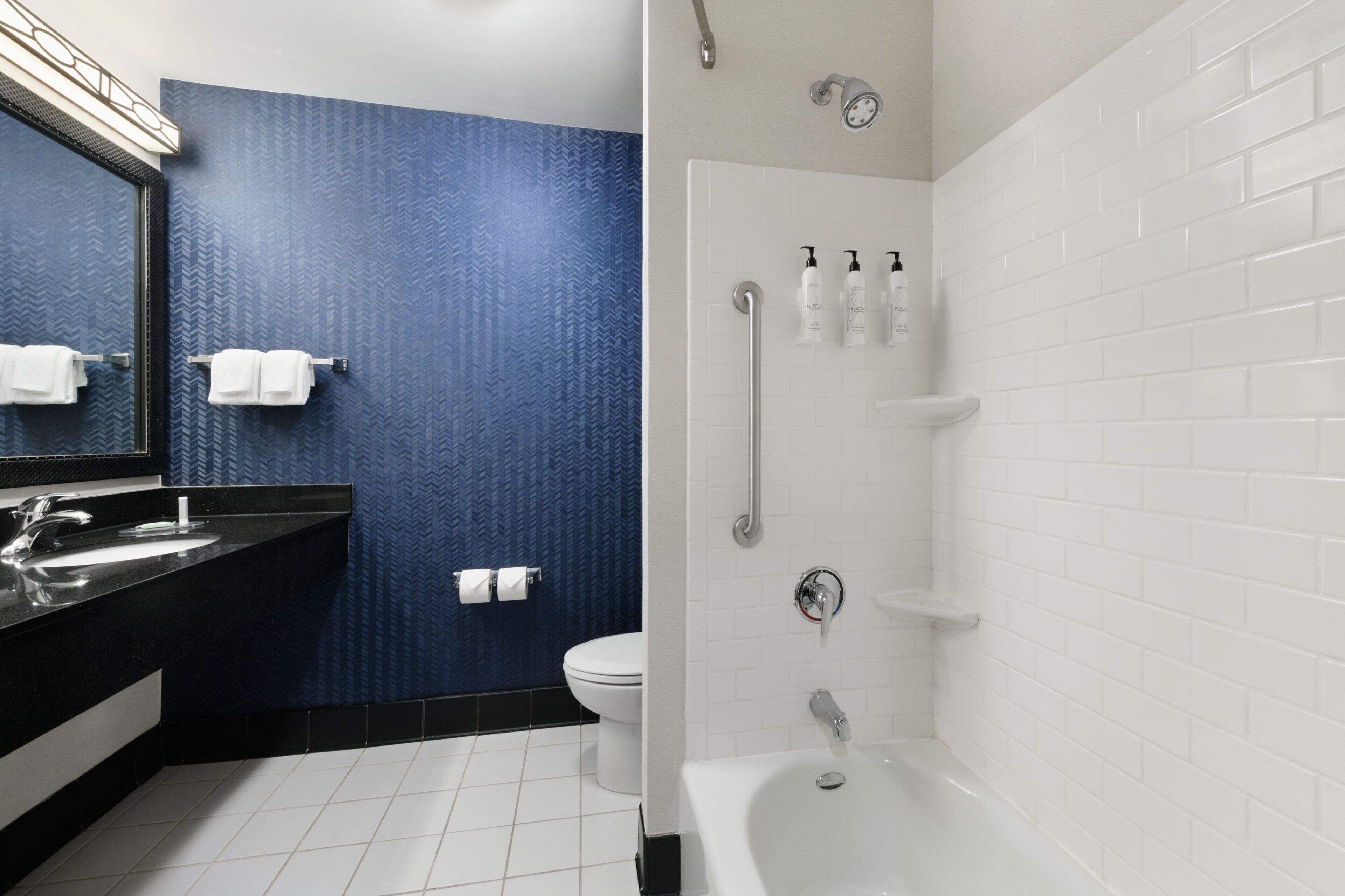 A modern bathroom with a black sink, white bathtub, and a blue textured wall.
