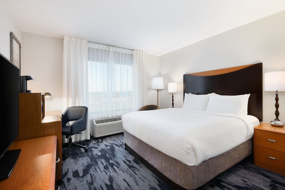 A hotel room with a large bed, a desk with a chair, a television, and a window with curtains.