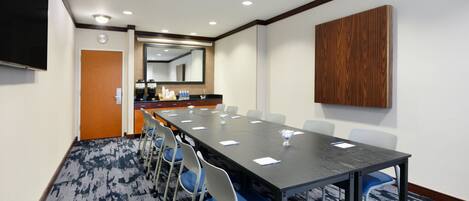 A conference room with a long table, chairs, a clock, a mirror, and a wooden panel on the wall.