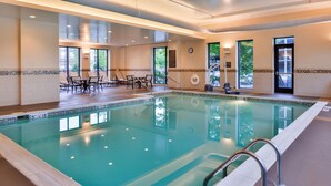 Una amplia piscina interior con agua cristalina, rodeada de sillones de descanso y una tumbona.