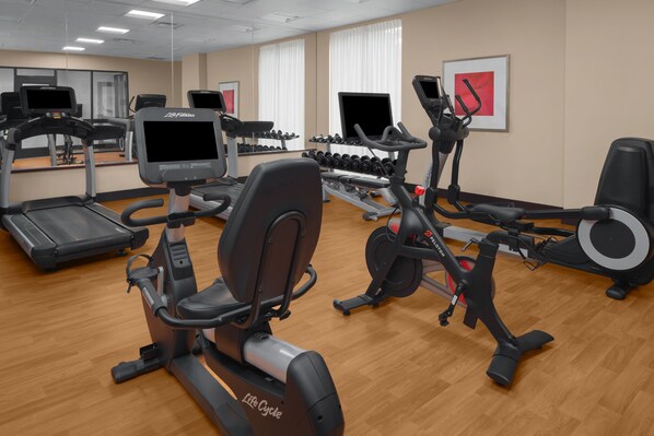 Une salle de sport équipée de tapis de course, de vélos elliptiques et d’haltères.