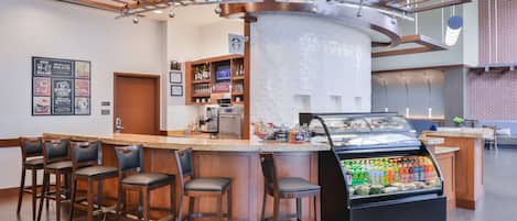 A bar area with a curved counter, bar stools, a beverage display, and a coffee menu on the wall.