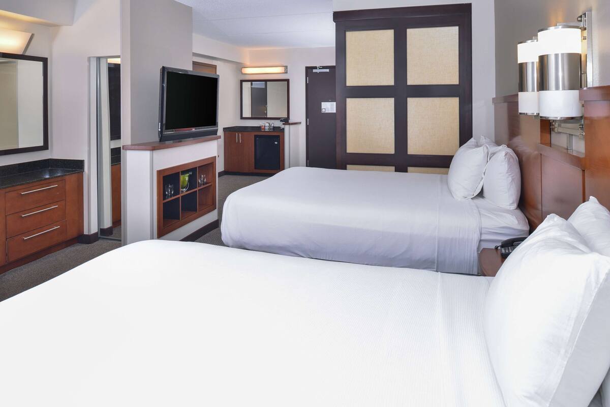 Ein Hotelzimmer mit zwei Betten, einem Fernseher, einer Minibar und einem Badezimmer.