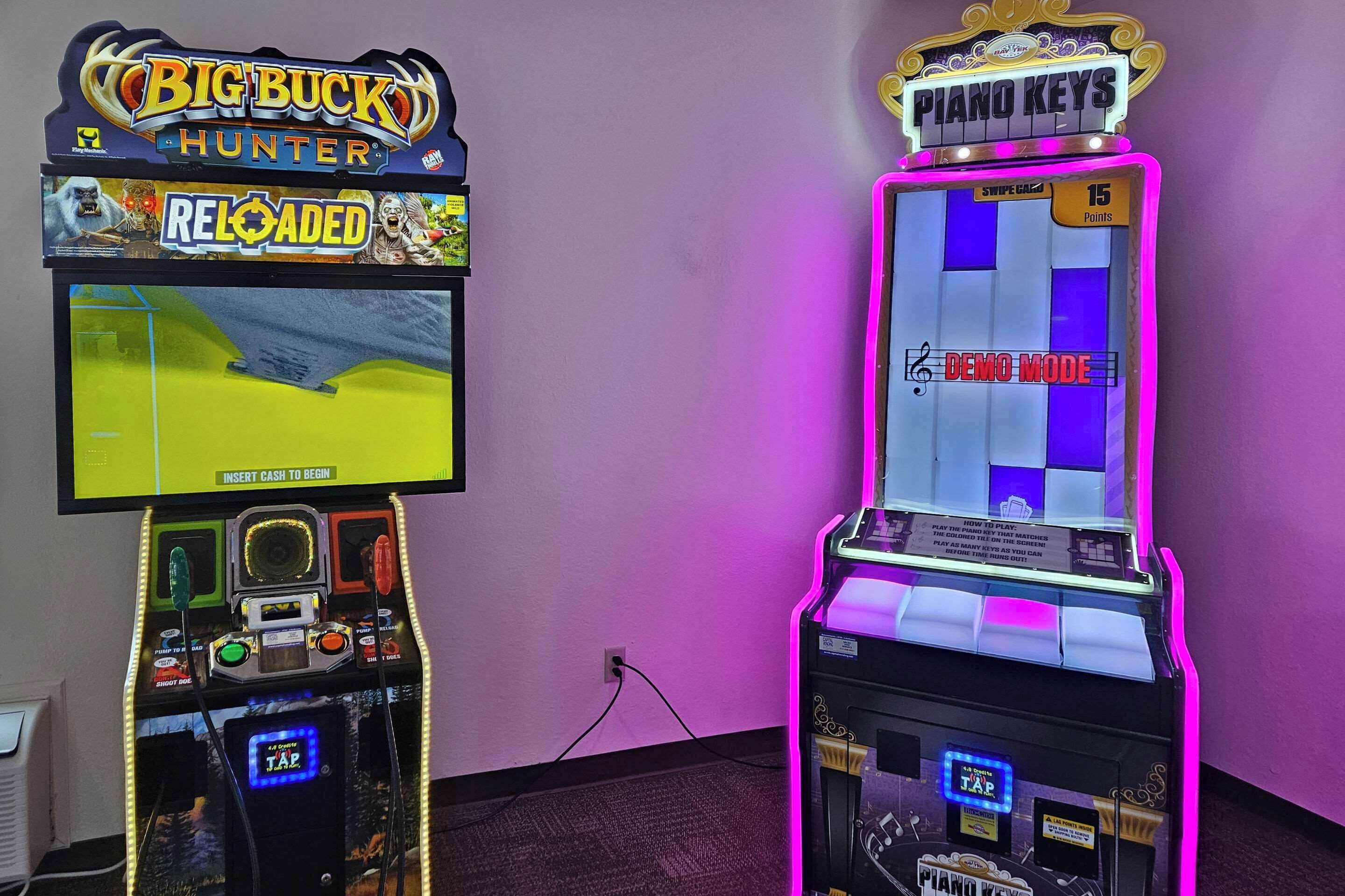 Two arcade machines, one for Big Buck Hunter and another for Piano Keys, with a purple wall in the background.
