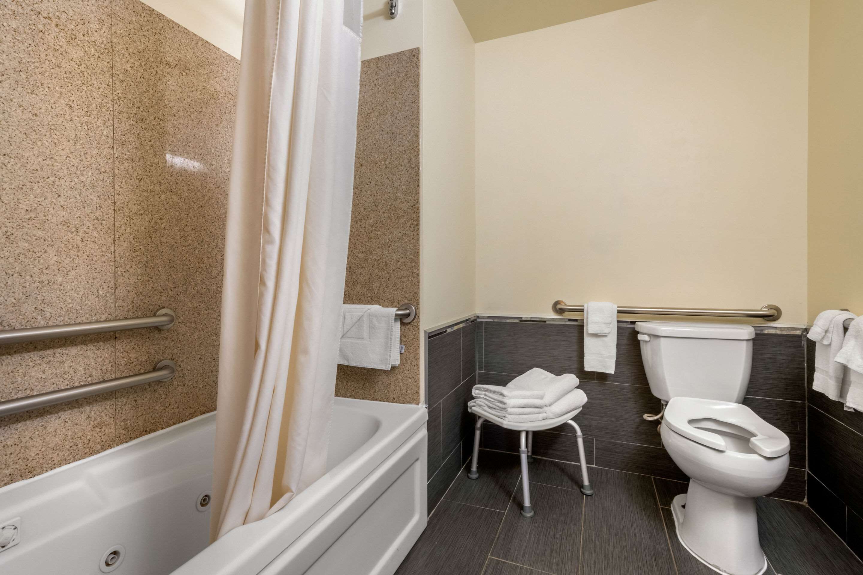 A bathroom with a bathtub, toilet, and handrails.