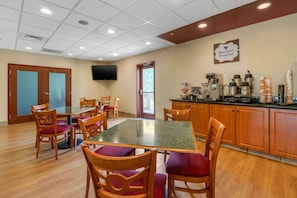 A dining area with wooden chairs and a glass table, a kitchen area with coffee machines, and a sign for MainStart Breakfast.