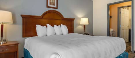 A hotel room with a large bed, two bedside tables with lamps, a framed picture on the wall, and a door leading to another room.
