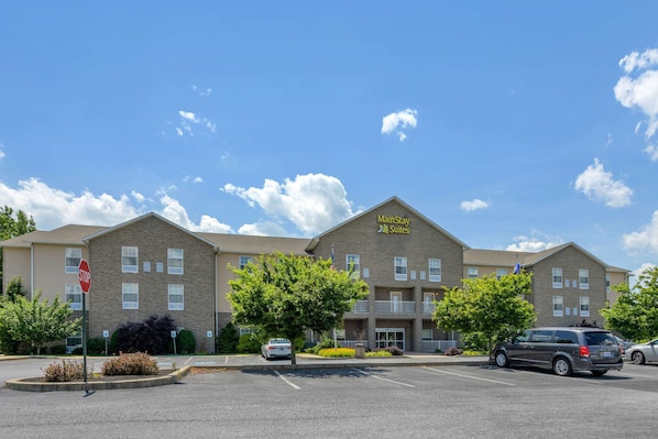 A MainStay Suites hotel with a parking lot, a stop sign, and a clear blue sky.