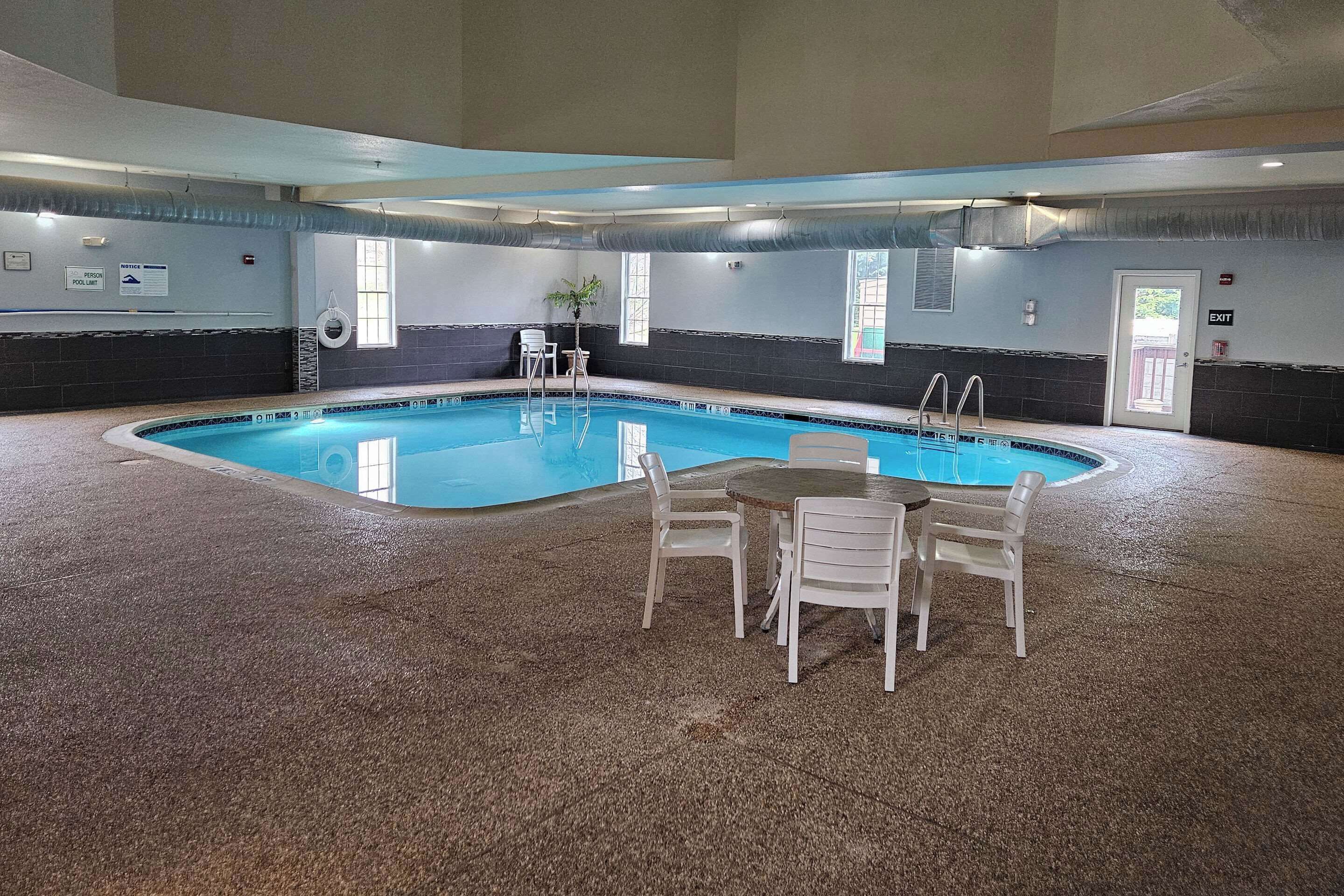 An indoor swimming pool with a tiled floor, a pool table, and a few chairs.