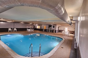 An indoor swimming pool with a heart-shaped design, surrounded by lounge chairs and a reception area.