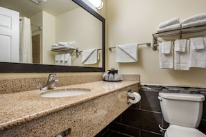 A bathroom with a granite countertop sink, a mirror, a towel rack with folded towels, and a toilet.