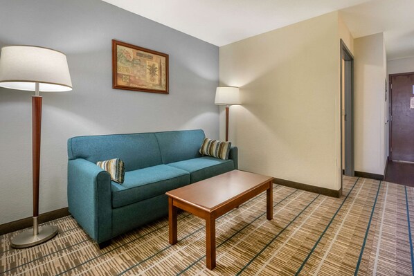 Habitación de hotel con un sofá azul, una mesa de centro de madera, dos lámparas de pie y una alfombra estampada.