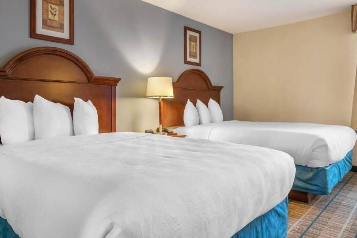 Ein Hotelzimmer mit zwei Betten, einem Nachttisch, einer Lampe und gerahmten Bildern an der Wand.