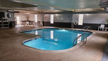 An indoor swimming pool with a tiled floor, a pool ladder, and a seating area with chairs and a table.