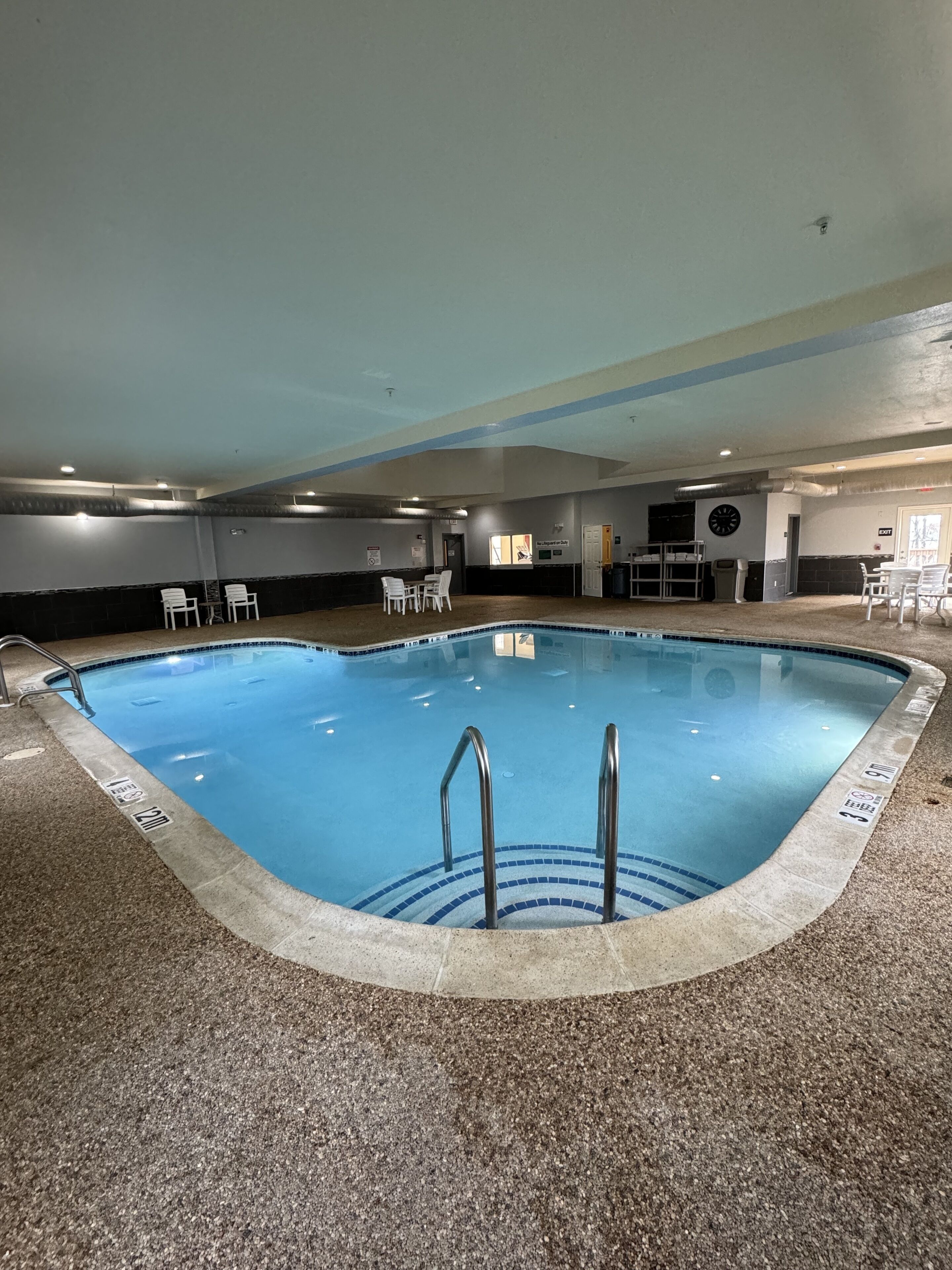 An indoor swimming pool with a clear water surface, a pool ladder, and a tiled floor.