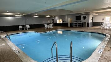 An indoor swimming pool with a clear water surface, a pool ladder, and a tiled floor.
