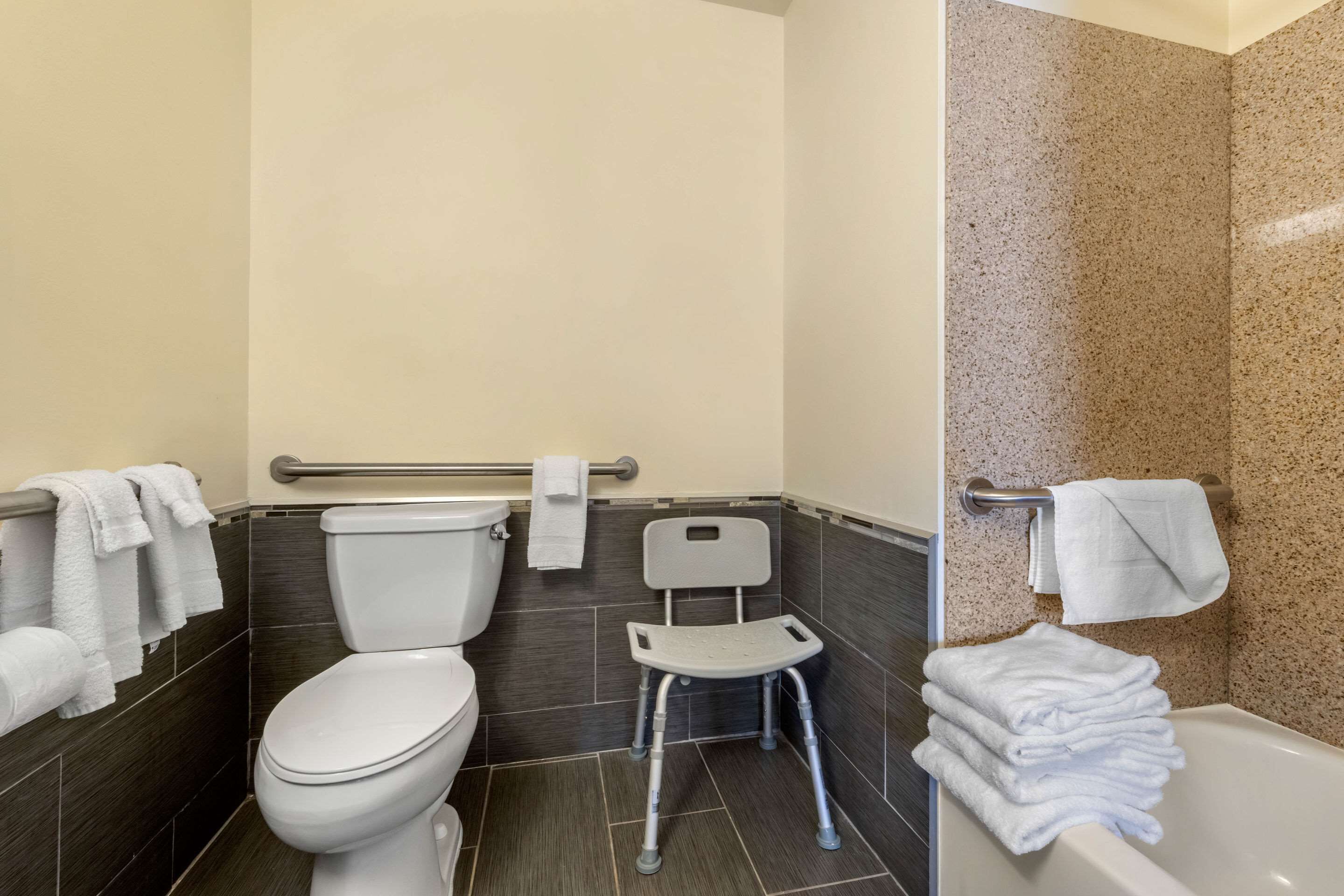 A bathroom with a toilet, a small chair, and a bathtub.