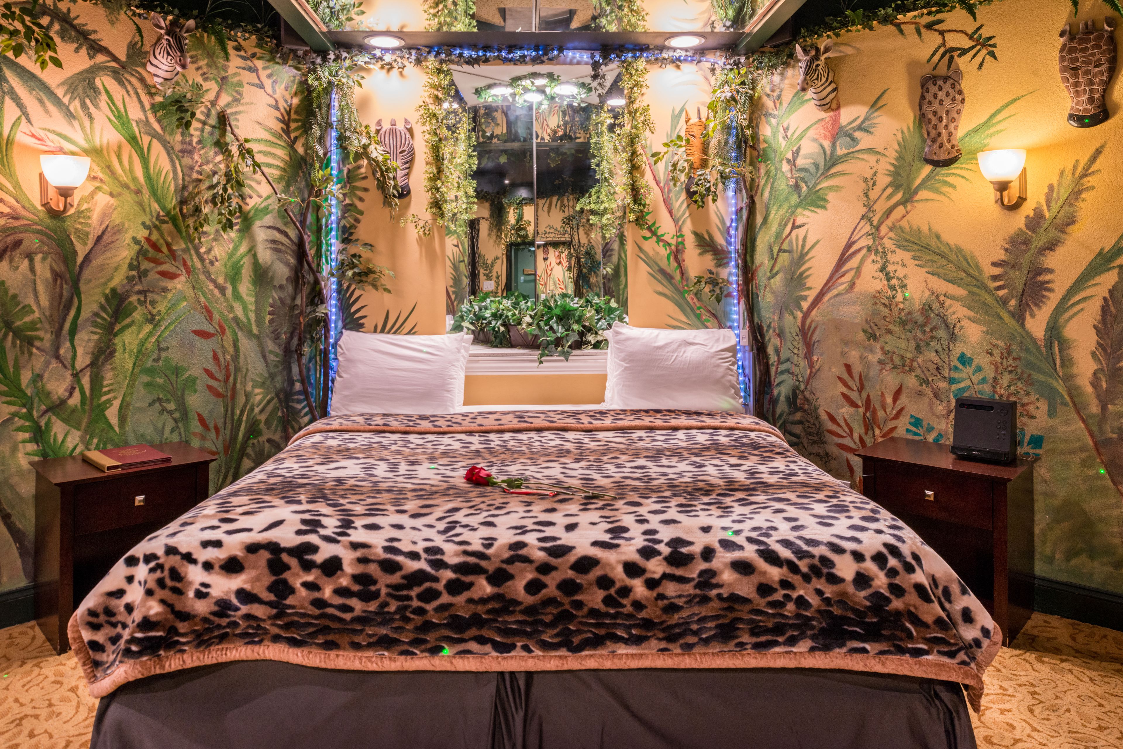 A room with a bed, two nightstands, a mirror, and a wall with a jungle-themed mural.